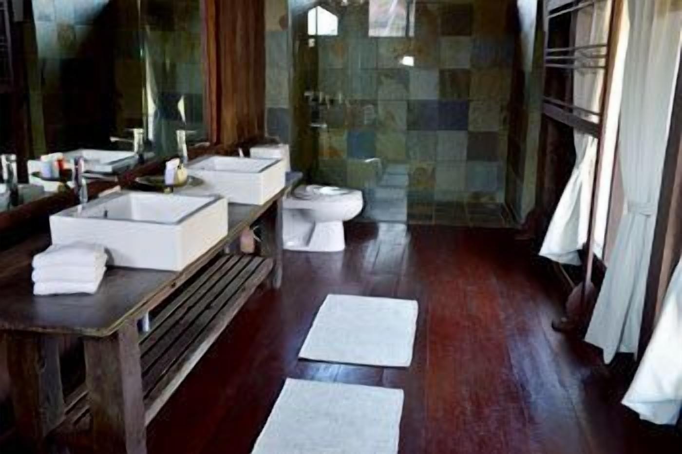 Un bagno con un mobile bagno in legno, due lavandini, un water e una zona doccia.