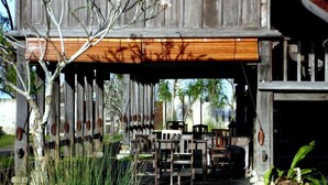A wooden structure with a covered outdoor seating area, including chairs and tables, and a potted plant. - Terrapuri Heritage Village (Setiu)