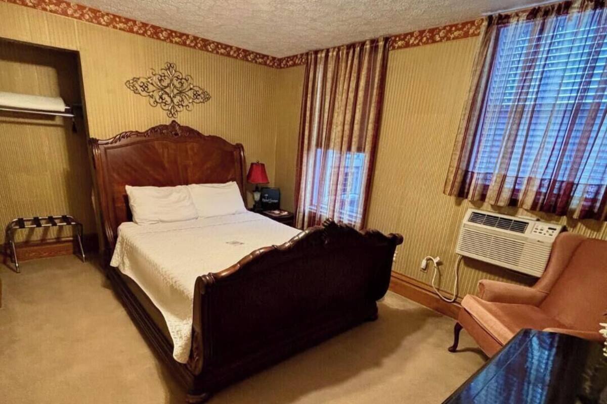 A bedroom with a wooden bed, a nightstand, a chair, a radiator, and a window with curtains.