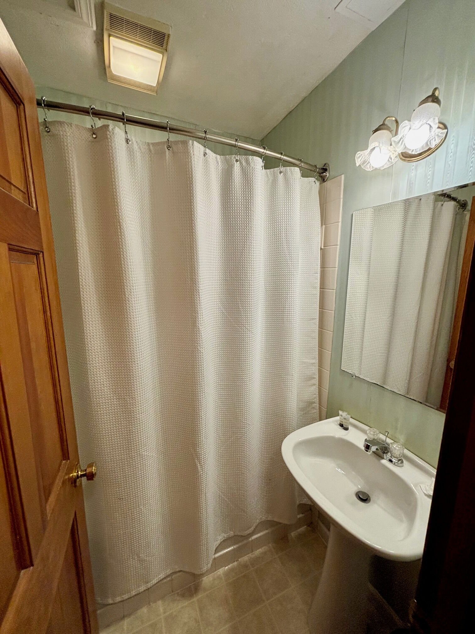 Un baño con cortina de ducha blanca, un lavabo y un espejo.