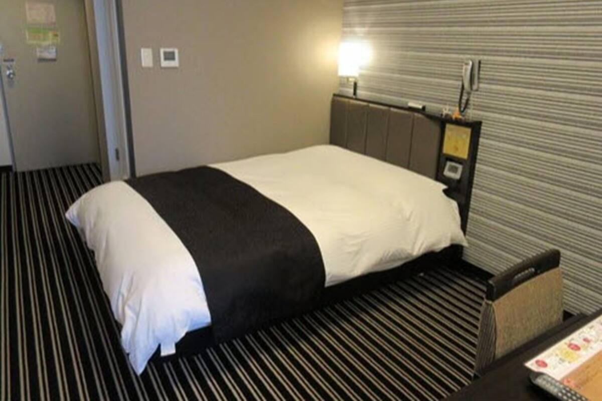 Una habitación de hotel con cama, mesita de noche, lámpara y alfombra a rayas.