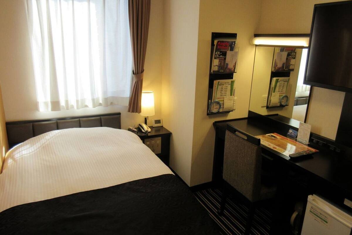 Habitación de hotel con cama, escritorio, computadora, teléfono y espejo.