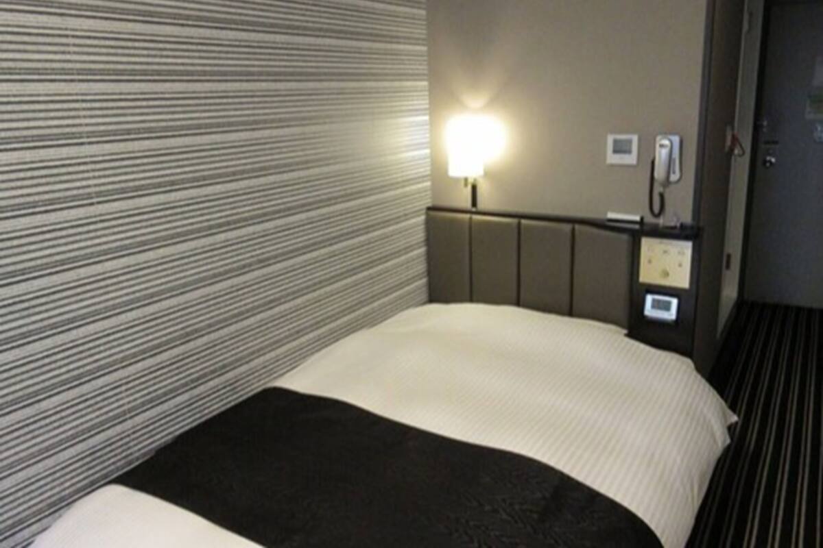 Una habitación de hotel con una cama, una mesita de noche con lámpara y un teléfono.