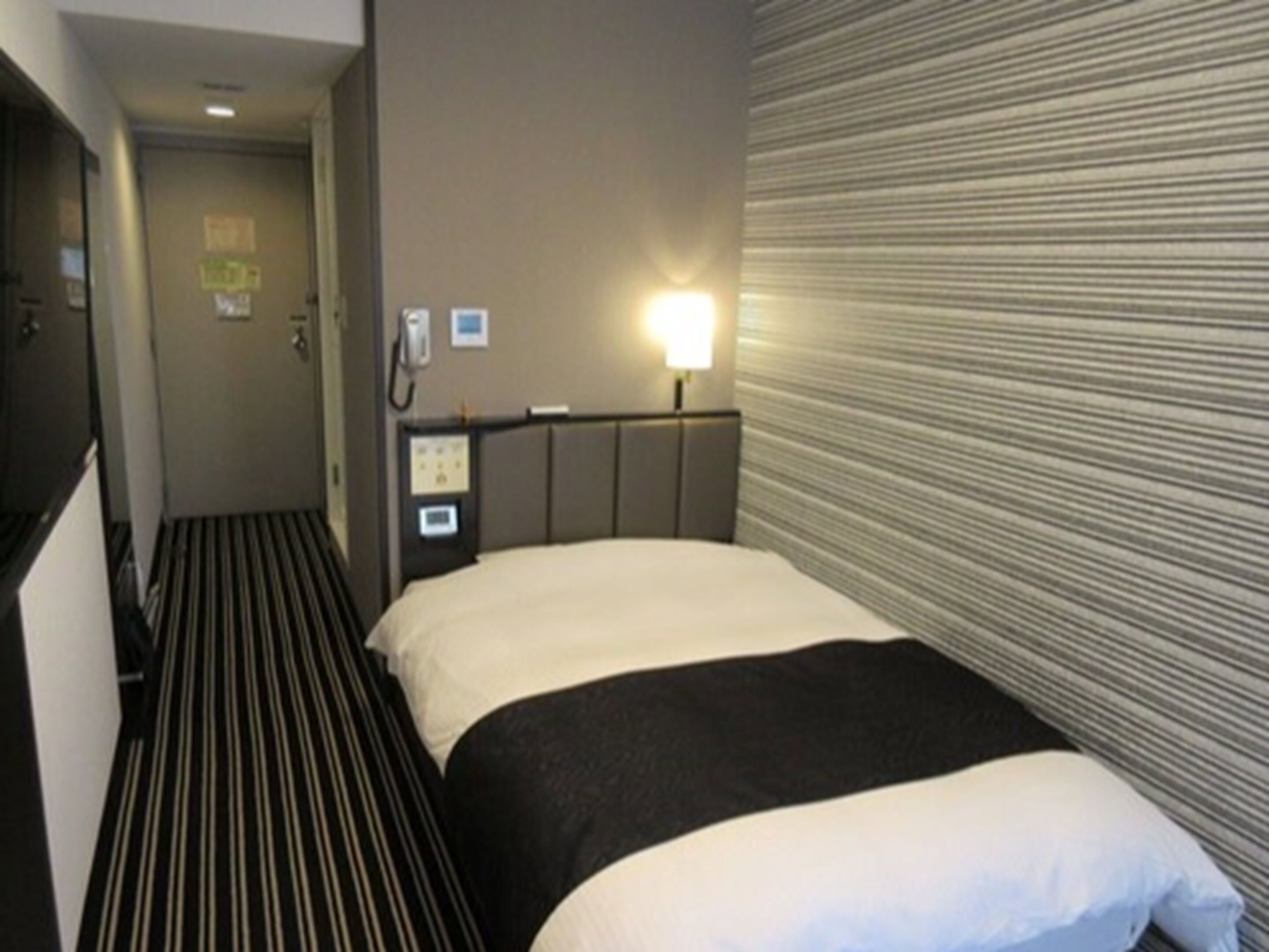 Una habitación de hotel con una cama, una mesita de noche, una lámpara y un teléfono.
