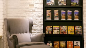 A room with a grey armchair and ottoman, a bookshelf with magazines, and a white brick wall. - York Design Hotel (Taipei)