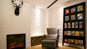 A room with a fireplace, a mounted deer head, a bookshelf with books, a grey armchair, and a wooden floor. - York Design Hotel (Taipei)