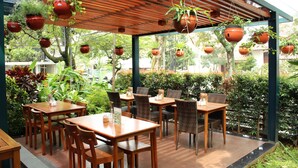 An outdoor restaurant with wooden tables and chairs, surrounded by hanging terracotta pots with plants. - Ivory Hotel Bandung (Bandung)
