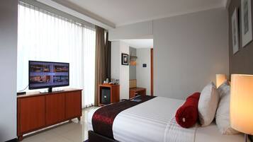 A hotel room with a large bed, a television on a wooden cabinet, a desk with a chair, and a window with curtains.