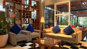 A spacious living area with a large bookshelf, two sofas with blue cushions, a coffee table, and a checkered floor. - Ivory Hotel Bandung (Bandung)