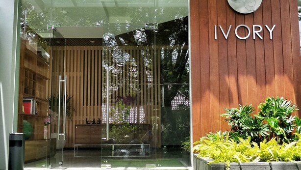 A modern building entrance with a glass facade, a wooden wall with the name 'IVORY', and a green lawn area. - Ivory Hotel Bandung (Bandung)