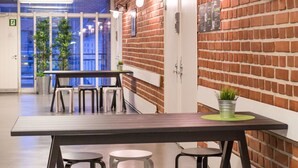 A modern interior with a brick wall, a long table with stools, and a clock. - Forenom Hostel Espoo Otaniemi (Espoo)