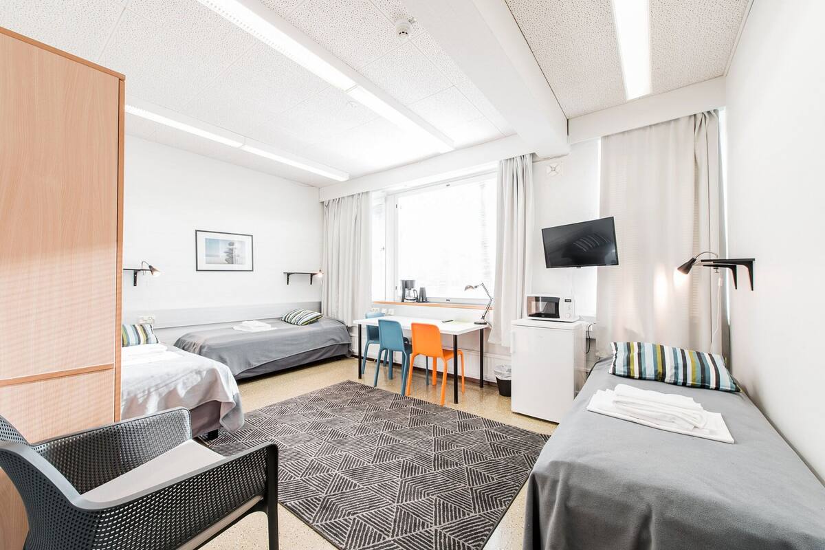 A modern hotel room with two beds, a desk, a TV, and a view of the city.
