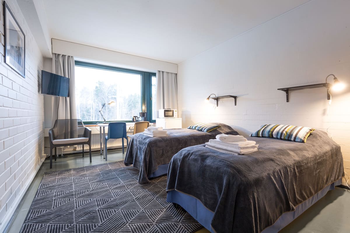 A hotel room with two beds, a desk, a chair, and a window with curtains.
