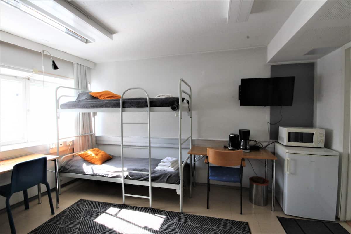 A dormitory room with bunk beds, a desk, a chair, a television, and a refrigerator.
