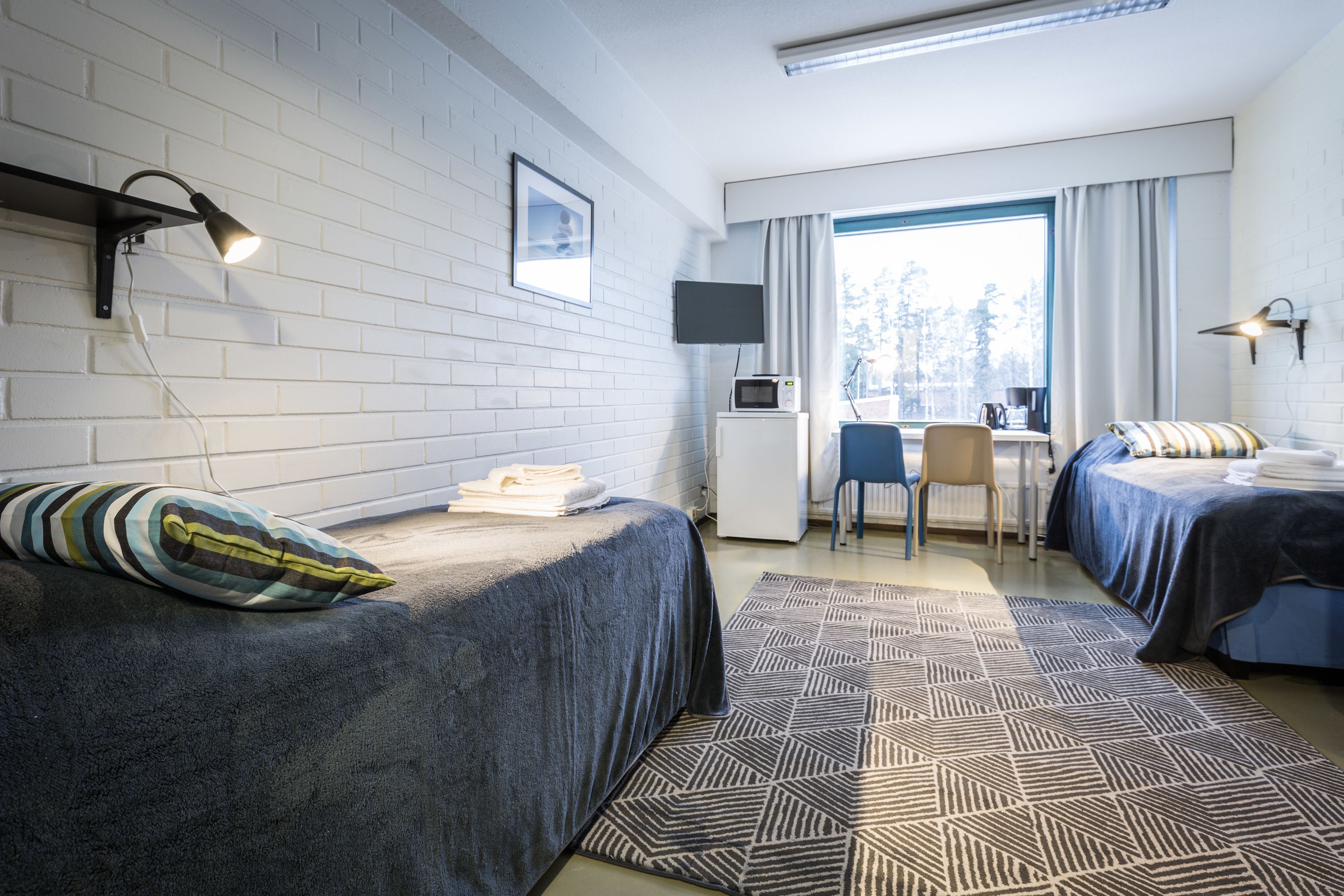 Een moderne hotelkamer met twee bedden, een bureau, een flatscreen televisie en een groot raam met gordijnen.