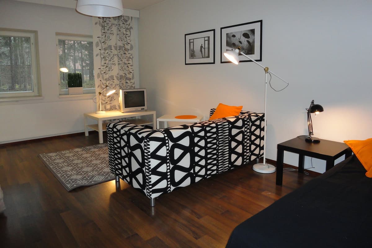 A modern living room with a patterned sofa, a small TV, a desk, and a lamp.