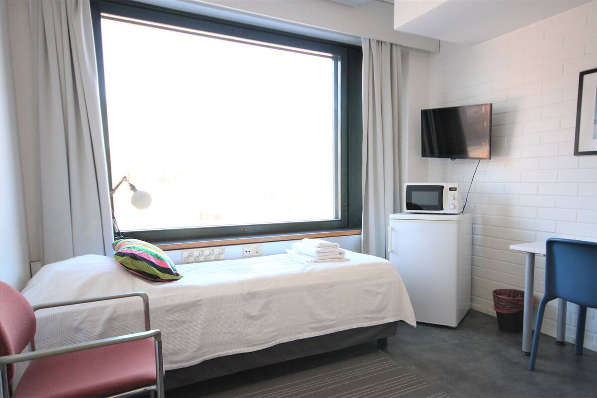 A hotel room with a bed, a desk, a chair, a TV, and a window with curtains.