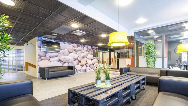 A modern lobby with a stone wall, comfortable seating, a wooden coffee table, and potted plants. - Forenom Hostel Espoo Otaniemi (Espoo)
