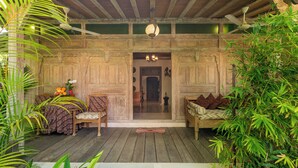 A wooden porch with a bench and a table with fruit, surrounded by plants. - Kampung Kecil (Denpasar)