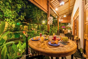 Un área de comedor al aire libre con piscina, rodeada de abundante vegetación y estructuras de madera.