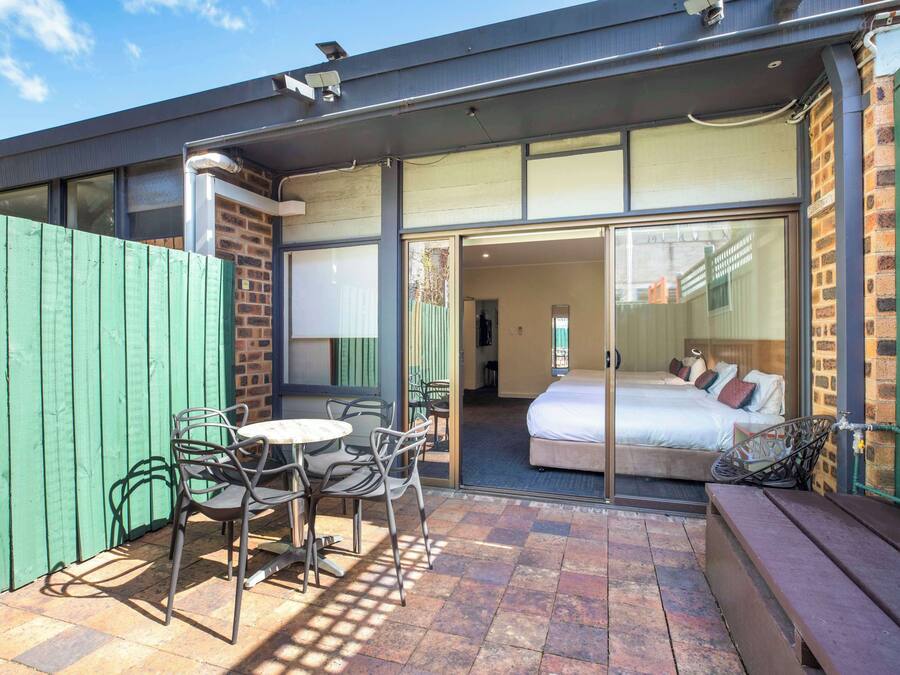 A room with a bed, a small table, and chairs, and a sliding glass door leading to another room.