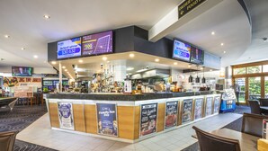 Un restaurante moderno con una barra central, varias pantallas mostrando contenido y diferentes opciones de asientos, incluyendo mesas y sillas.