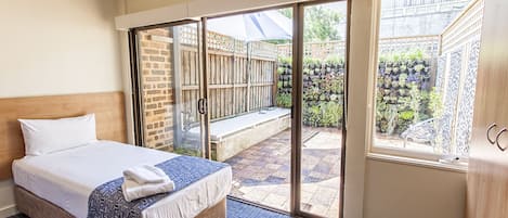 A hotel room with a bed, a sliding glass door to a patio, and a view of a garden.