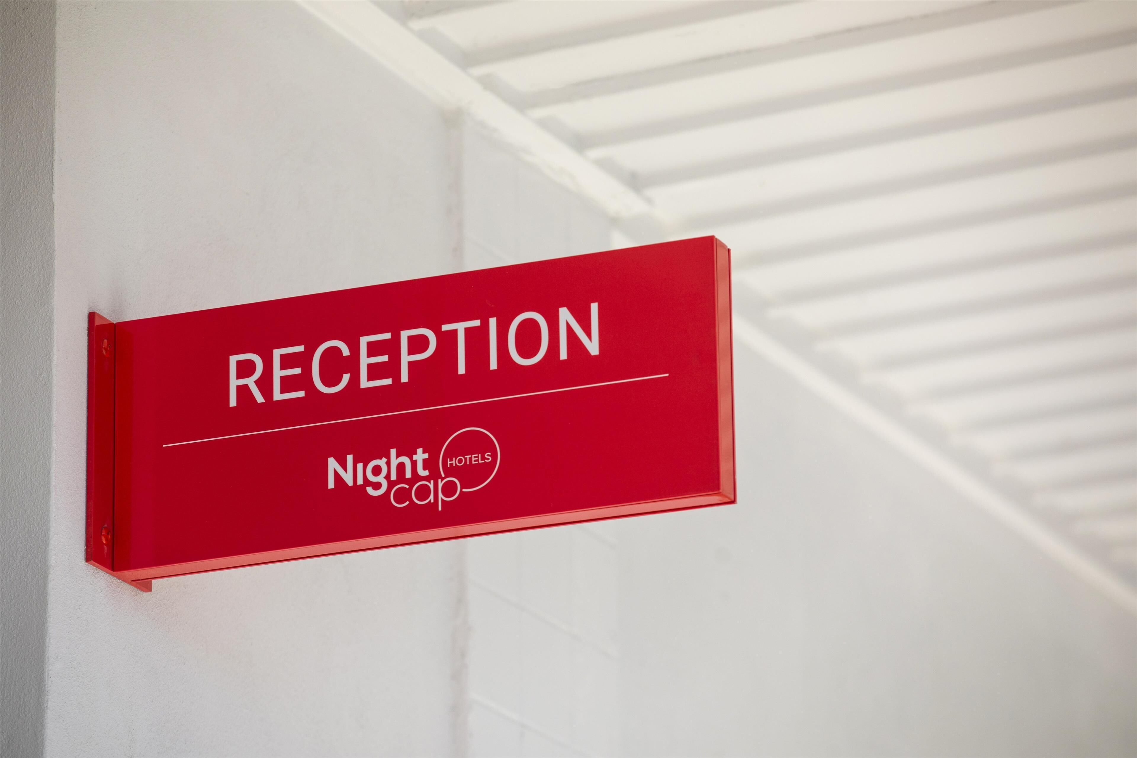Un panneau rouge indiquant la réception, avec les inscriptions « RÉCEPTION » et « Nightcap Hotels ».