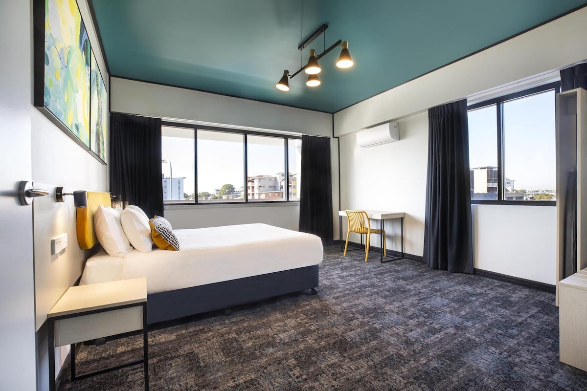A modern hotel room with a large bed, a desk, and a view of the city.