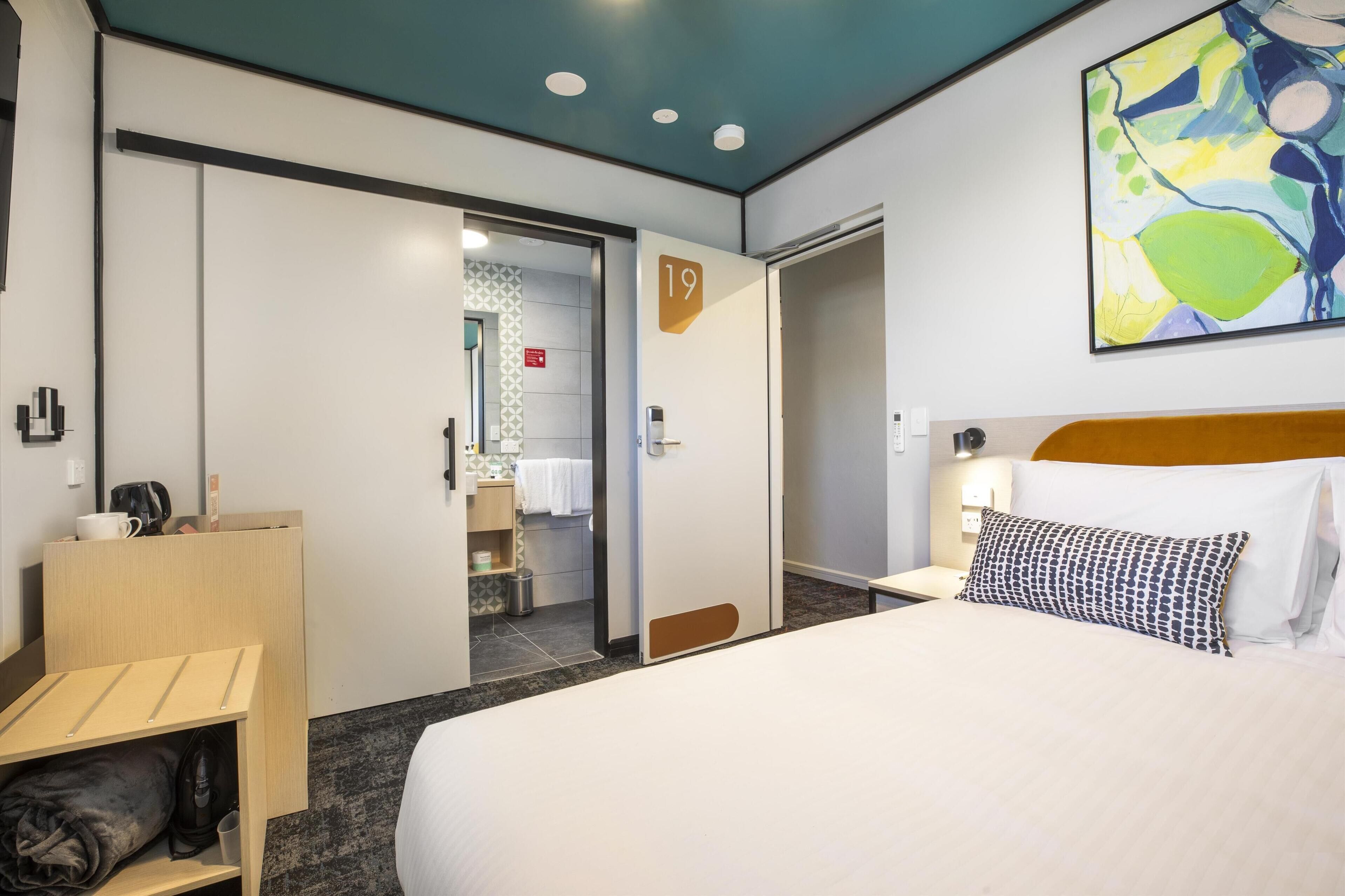 Habitación de hotel con cama, escritorio, armario y baño visible a través de una puerta abierta.