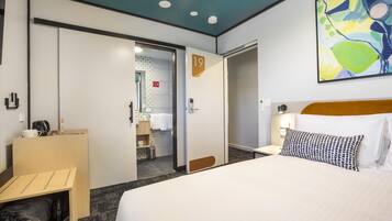 Habitación de hotel con cama, escritorio, armario y baño visible a través de una puerta abierta.