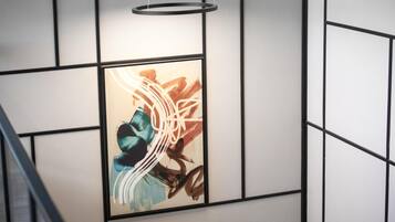 A modern interior with a geometric wall design, a framed abstract painting, and a hanging light fixture.