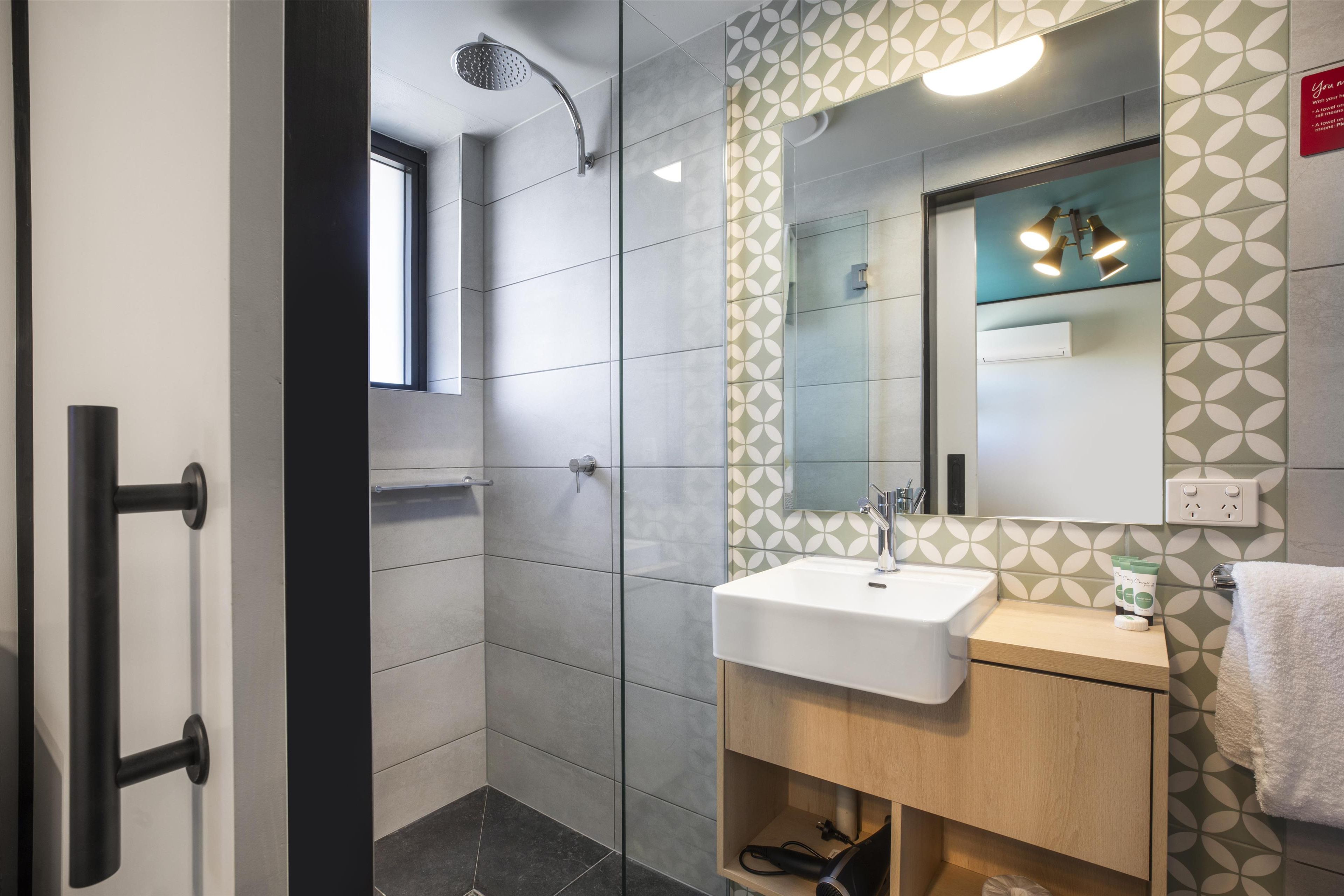A modern bathroom with a glass shower enclosure, a white sink, and a wooden vanity.