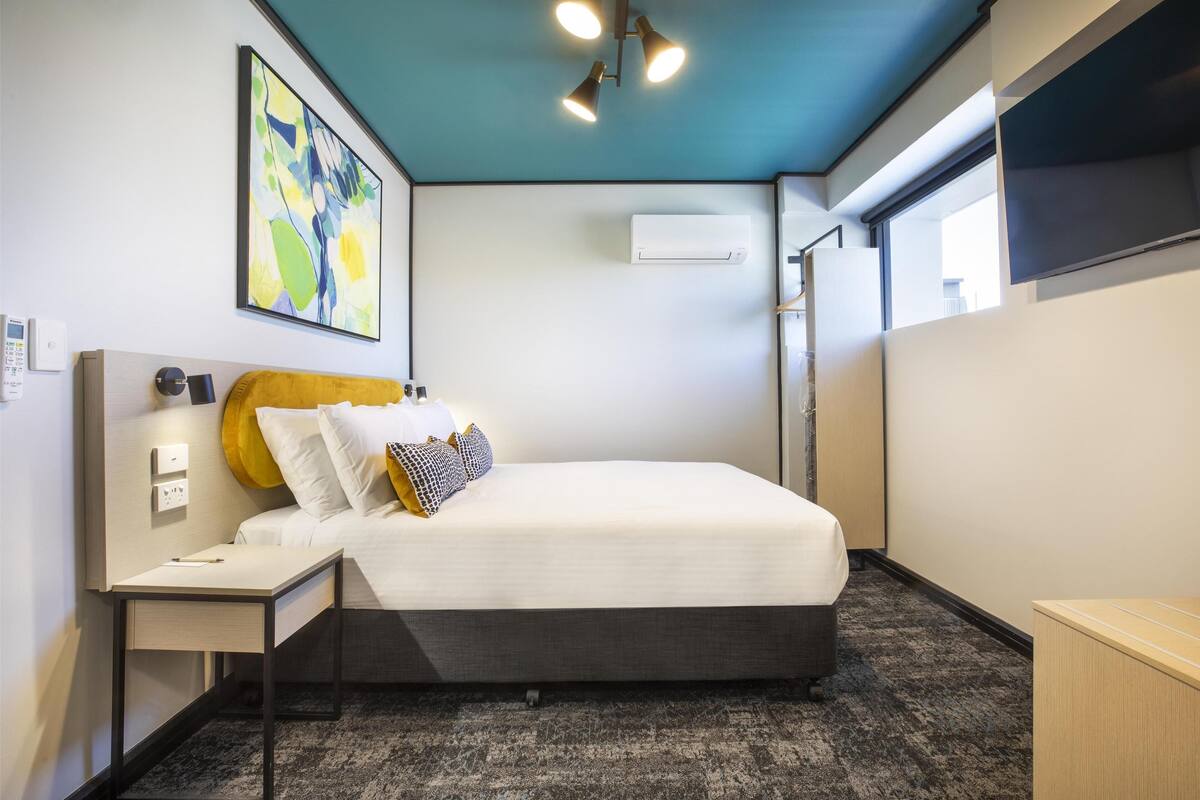 A modern hotel room with a bed, bedside table, and a wall-mounted air conditioner.