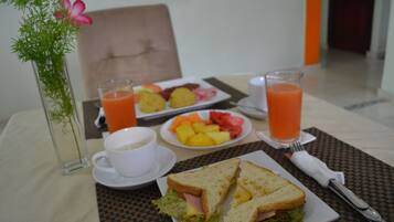A breakfast setting with a plate of fruit, two glasses of orange juice, a cup of coffee, and a sandwich on a table.