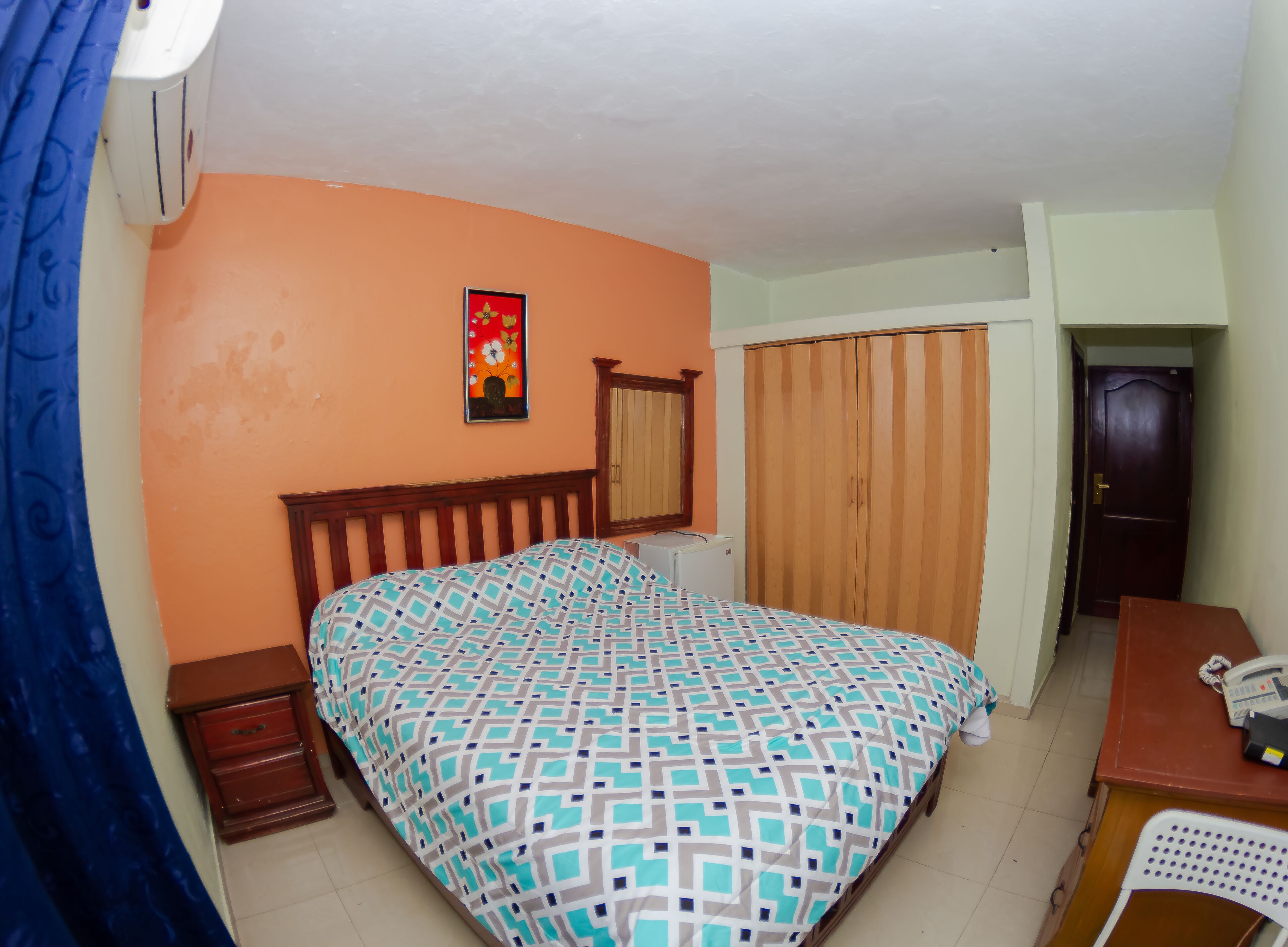Une chambre à coucher avec un lit, une armoire en bois, un bureau avec un téléphone et un miroir au mur.