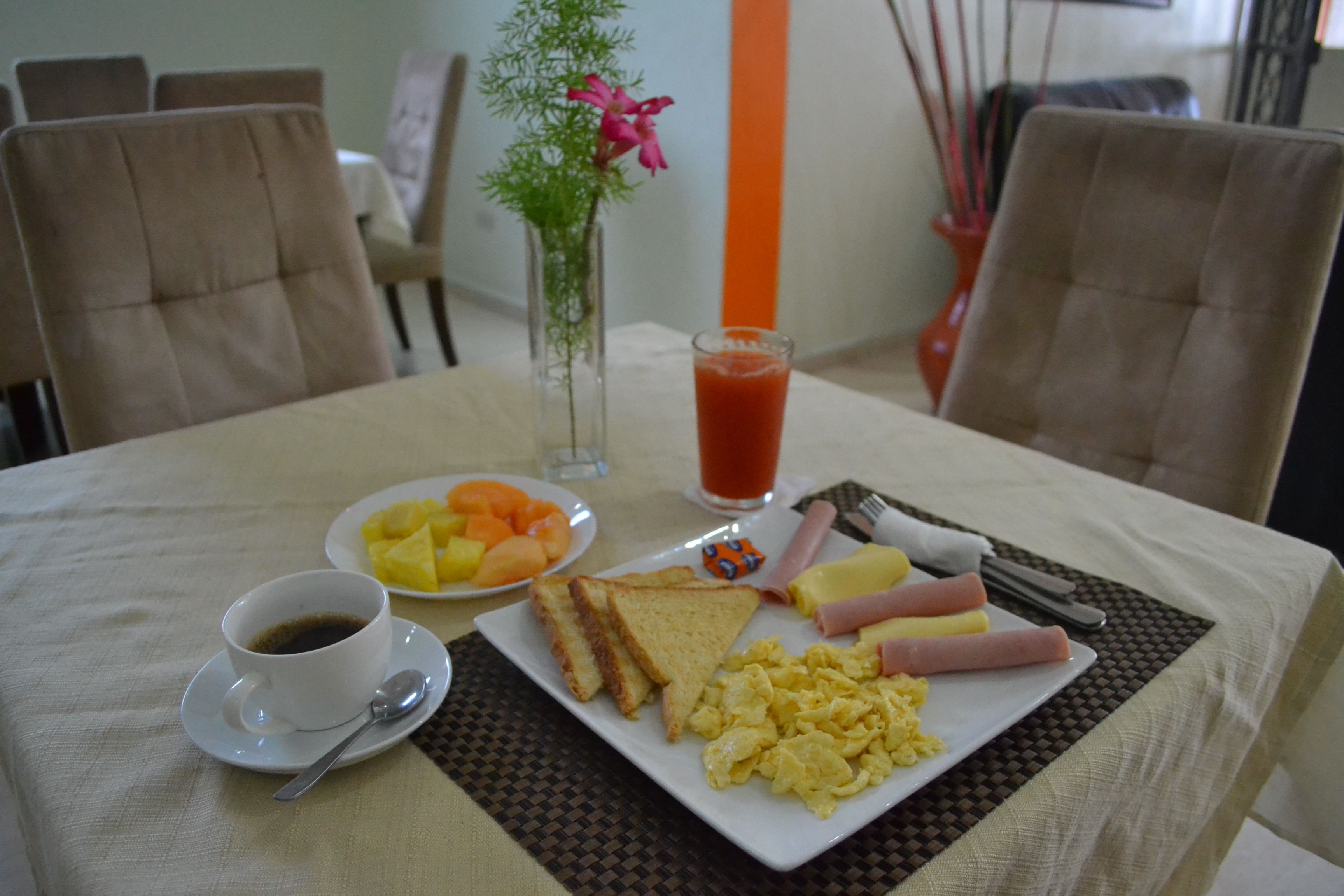 A breakfast table with a plate of toast, eggs, sausages, and a cup of coffee.