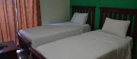 Two single beds with wooden headboards in a room with green walls and a window with orange curtains.