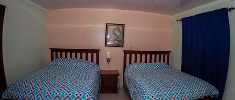 A room with two beds, a nightstand, a wall-mounted lamp, and a framed picture.
