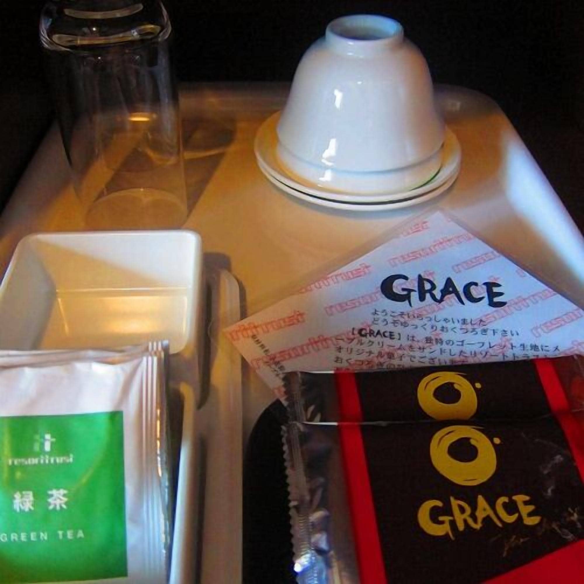 A tray with a white cup, a glass, a white box, and a green tea packet.