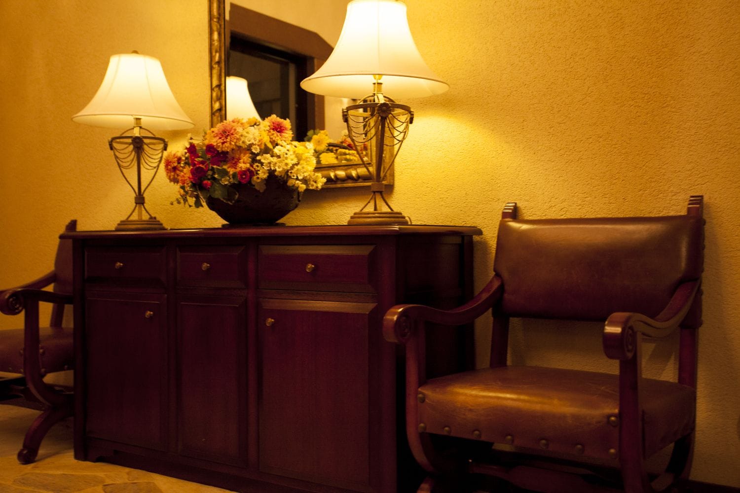 Un bureau en bois, avec deux lampes, un vase de fleurs et un miroir accroché au mur.