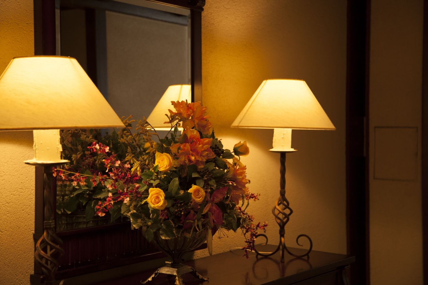 Een kamer met een tafellamp, een spiegel en een bloemstuk.