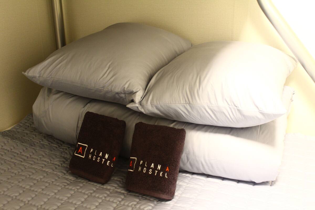 Sängyllä on kaksi tyynyä ja kaksi taitetusti asetettua pyyhettä, ja sängyn päällä on kuvioitu peitto.