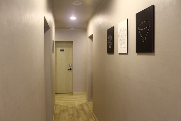 A hallway with a wooden floor, a door at the end, and three framed artworks on the wall.