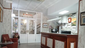 A hotel lobby with a reception desk, seating area, and a staircase leading to the upper floors. - Hotel Royal (Ronda)