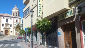 A street view with Hotel Royal signage, a building with a bell tower, and a palm tree. - Hotel Royal (Ronda)