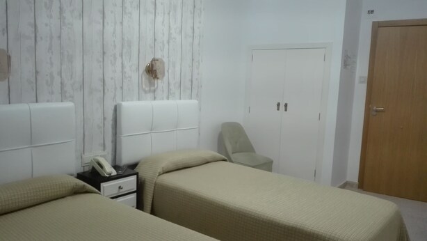 A bedroom with two single beds, a bedside table with a phone, a chair, and a wardrobe. - Hotel Royal (Ronda)