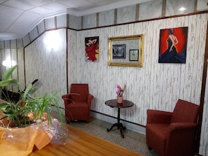 A room with two red armchairs, a small round table with a pink vase, and a potted plant on a wooden table. - Hotel Royal (Ronda)