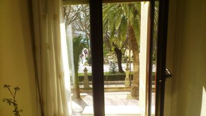 A room with a sliding glass door leading to an outdoor area with a palm tree and a fence. - Hotel Royal (Ronda)