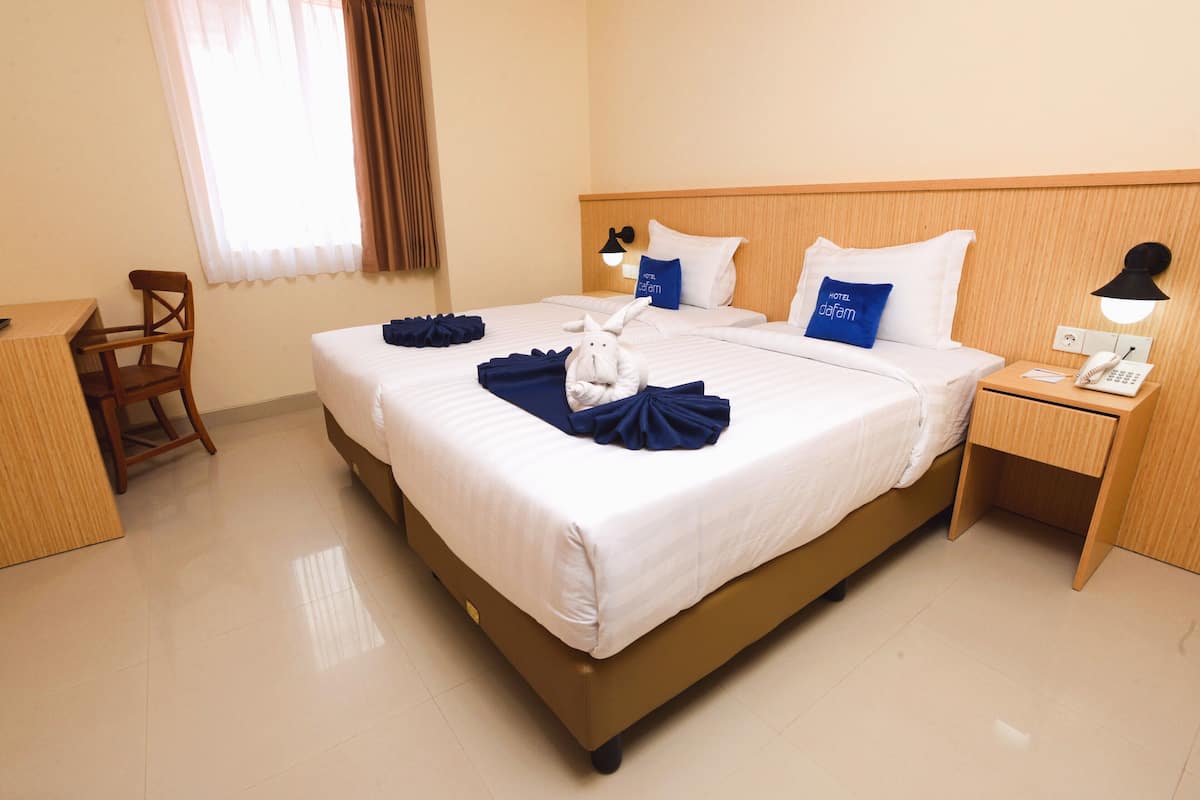 A hotel room with a large bed, a desk, a chair, and a nightstand with a lamp and phone.